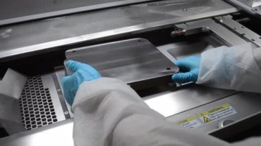 Laboratory worker in white protective suit and gloves installing metal platform on work surface of large industrial metal 3D printer. 3D printer for printing metal objects from metal powder inside
