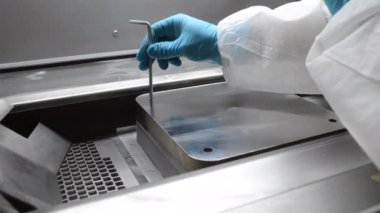 Laboratory worker in white protective suit and gloves installing metal platform on work surface of industrial metal 3D printer. 3D printer for printing objects from metal powder inside. Tighten nuts
