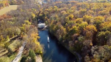 Beautiful panoramic autumn landscape park, many trees with yellow leaves, lake with fountain in center, architecture, big stones, paths walkways, people walking on sunny autumn day. aerial drone view