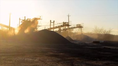 Mining quarry. Crushing plant in granite quarry at sunset dawn. Lot of dust. Industrial production of gravel. Gravel conveyor. Cone type rock crusher. Stone crushing. Crusher in quarry. Shining sun.