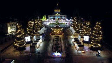 Kyiv, Ukrayna 20 Ocak 2022: Manzara manzarası büyük bina, Noel ağaçları, çocuk atlıkarınca ve açık hava buz pateni pisti. Parlak süslemeler, çelenkler, aydınlatma Yeni Yıl Noeli