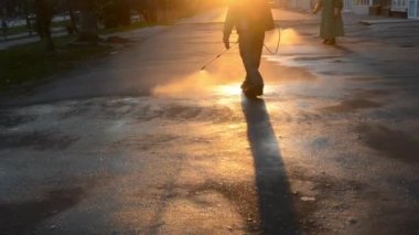 Man in airtight suit sprays disinfecting liquid pavement on street in city on backdrop of sunset. Sanitation workers clean crosswalk. Sanitary measures. Sanitation of city street. Coronavirus pandemic