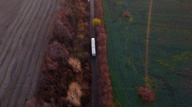 Büyük beyaz kargo kamyonu ve beyaz araba tarla arazileri arasında toprak yol kullanıyor. Üst manzara, hava aracı görüntüsü. Nakliye teslimatı, kargo taşımacılığı.