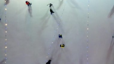 People skating on ice skating rink outdoors on winter night top view. Luminous glowing garlands lamps lighting. Lowering down. Aerial drone view. New Year Christmas celebration holidays recreation.