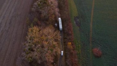 Large white cargo truck and white car driving dirt road between agricultural fields countryside. Top view, aerial drone view. Transport transportation delivery shipping, freight cargo transportation