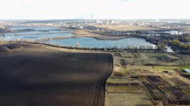 Urban beautiful landscape agricultural plowed fields, lakes for growing fish, gardens, thermal power plant, building industrial area of city, cloud shadows on sunny autumn day. Aerial drone view.