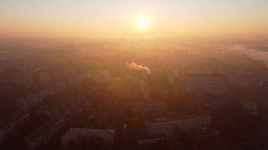 Beautiful cityscape in summer at sunrise. Flying over many multi-storey buildings and a chimney with white smoke. Bright shining sun. Urban landscape. Dawn sunrise dawning sunset sundown, rising sun.