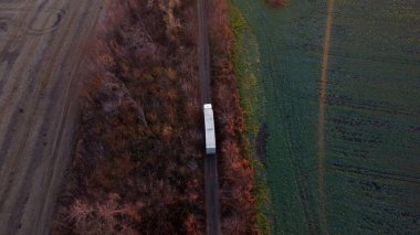 Large white cargo truck driving dirt road between agricultural fields countryside. Top view, aerial drone view. Transport transportation delivery shipping, freight transportation,cargo transportation