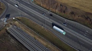 Otoyol, arabalar, tarım tarlaları, güneşli bir sonbahar gününde hasattan sonra. Üzerinde beyaz işaretler ve bir sürü araba olan asfalt yolda uçuyorlar. Hava aracı görünümü