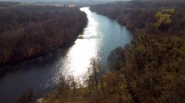 Panoramik doğal manzara. Nehir, güneş suyun yüzeyinde parlıyor, güneşli bir sonbahar gününde ağaçlar kıyılarda. Nehrin su yüzeyinde güneş ışığıyla uçuyor. Hava aracı görüntüsü. Doğa manzarası