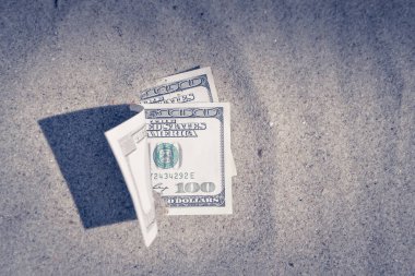 Paranın yarısı kumla kaplı, yakın planda yatıyor. Dolar banknotları kısmen kuma gömülmüş. Okyanus sahilinde kumlara gömülü 300 dolar. Finans parası hariç. Tatilde rahatla.