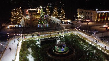 Birçok insan açık havada buz pateni pistinde paten kayıyor. Yılbaşı süsleri, süslemeler, kış gecelerinde parlak çelenkler. Yeni yıl Noel kutlaması. Havadan