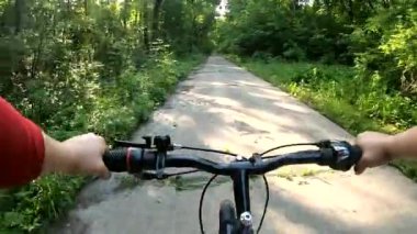Güneşli yaz gününde yeşil ormanda beton yol boyunca bisiklet süren bir kadın. Bisiklet süren bir adam. Bakış açısı. Spor, aktif eğlence, eğlence, dinlenme, rahatlama, seyahat, eğlence, turizm