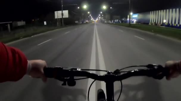 男人骑自行车在一个汽车道路上在城市的夜晚 晚上骑着一辆自行车在马路中间穿过城市 晚上在城里骑车 铺面公路白色标记 Pov — 图库视频影像