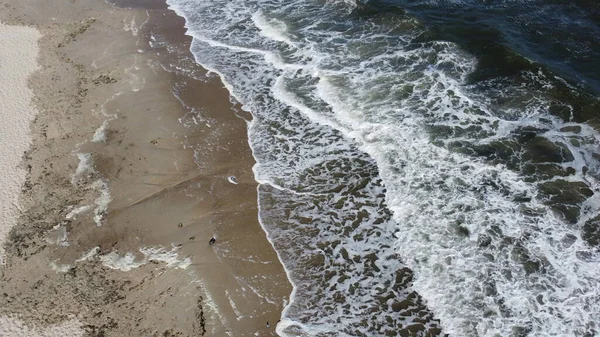 Sea waves from above. Sea waves with white foam rolling on sandy beach of the seashore coast on sunny day. Flying over sandy beach. Top view. View from above. Seascape waterscape. Aerial drone view