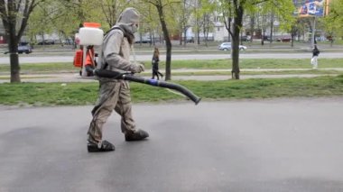 Koruyucu giysili bir adam şehrin kaldırımına antiseptik solüsyon sıkıyor. Koronavirüsü önlemek için sprey kimyasalların dezenfekte edilmesi. Halka açık yerlerde hijyenik önlemler. Koronavirüs salgını