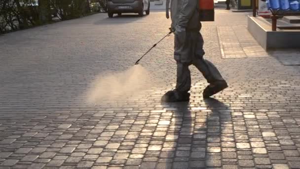 街の歩道で防腐剤の溶液を噴霧保護スーツの男 拡散コロナウイルスを防ぐためにスプレー化学薬品を消毒するペルソナ 公共の場での衛生対策 コロナウイルスのパンデミック — ストック動画