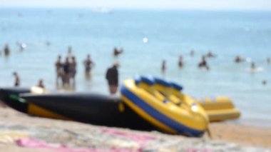 Bulanık arka plan deniz kumsalı. Birçok insan güneşli yaz gününde şişirilebilir tekne gezintisi yapar. İnsanlar deniz kıyısında yüzerek dinleniyor. Tatil kavramı, tatil seyahatleri, dinlenme, tatil ve tatil.