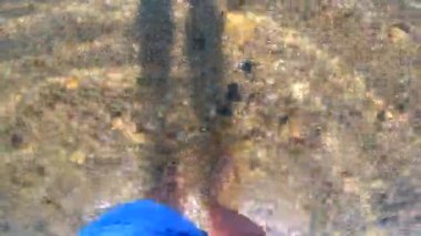 Kadın denizin kumlu tabanında çıplak ayakla yürüyor. Taşlar, kabuklar, şeffaf su ve akan suyla. Bakış açısı. Üst Manzara. dinlenme, rahatlama, seyahat, turizm, dinlenme, keyif