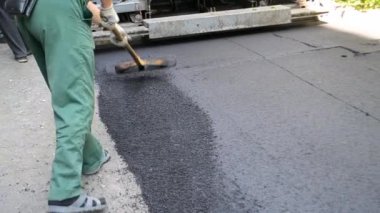 Büyük asfalt kaldırım makinesi ve insanlar. Paver kaldırım makinesi. Asfaltı düzleştiren bir işçi. Asfalt asfalt kaldırım makinesi caddede asfalt yuvarlıyor. Paving ekipmanları. Püskürtme basınç makinesini çökertir