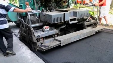 Büyük asfalt kaldırım makinesi ve insanlar. Paver kaldırım makinesi. Asfaltı düzleştiren bir işçi. Asfalt asfalt kaldırım makinesi caddede asfalt yuvarlıyor. Paving ekipmanları. Püskürtme basınç makinesini çökertir