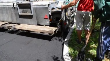 Büyük asfalt kaldırım makinesi ve insanlar. Paver kaldırım makinesi. Asfaltı düzleştiren bir işçi. Asfalt asfalt kaldırım makinesi caddede asfalt yuvarlıyor. Paving ekipmanları. Püskürtme basınç makinesini çökertir