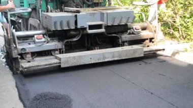 Büyük asfalt kaldırım makinesi ve insanlar. Paver, kaldırım makinesi. Büyük, eski asfalt asfalt asfalt makinası sokakta sıcak siyah asfalt yuvarlıyor. Asfalt kaldırım ekipmanları. Püskürtme basınç makinesini çökertir