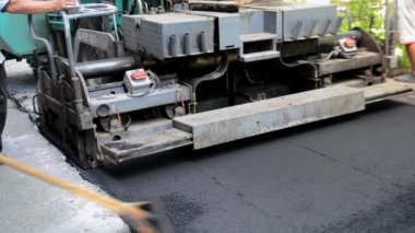 Büyük asfalt kaldırım makinesi ve insanlar. Paver kaldırım makinesi. Asfaltı düzleştiren bir işçi. Asfalt asfalt kaldırım makinesi caddede asfalt yuvarlıyor. Paving ekipmanları. Püskürtme basınç makinesini çökertir