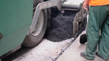 Asfalt asfalt dökerken asfalt tozu dökülüyor. Büyük kaldırım makinesi ve işçiler. Caddede asfalt gibi dönen bir makine. Aspirasyon aletleri. Püskürtme basınç makinesini çökertir