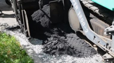 Asfalt asfalt dökerken asfalt tozu dökülüyor. Büyük kaldırım makinesi ve işçiler. İşlem makinesi yolda asfalt yuvarlıyor. Aspirasyon aletleri. Basınç makinesini döndürür