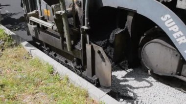 Asfalt asfalt dökerken asfalt tozu dökülüyor. Büyük kaldırım makinesi ve işçiler. İşlem makinesi yolda asfalt yuvarlıyor. Aspirasyon aletleri. Basınç makinesini döndürür