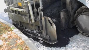 Asfalt asfalt dökerken asfalt tozu dökülüyor. Büyük kaldırım makinesi ve işçiler. İşlem makinesi yolda asfalt yuvarlıyor. Aspirasyon aletleri. Basınç makinesini döndürür
