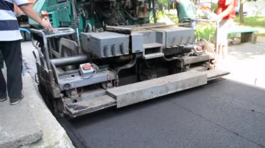 Büyük asfalt kaldırım makinesi ve insanlar. Paver kaldırım makinesi. Asfaltı düzleştiren bir işçi. Asfalt asfalt kaldırım makinesi caddede asfalt yuvarlıyor. Paving ekipmanları. Püskürtme basınç makinesini çökertir