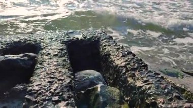 Deniz dalgaları güneşli bir yaz gününde kıyıda eski beton levhalara vurur. Beyaz köpüklü mavi deniz dalgaları. Deniz manzarası işte. Deniz kıyısı kıyısı. Doğal zemin arkaplan