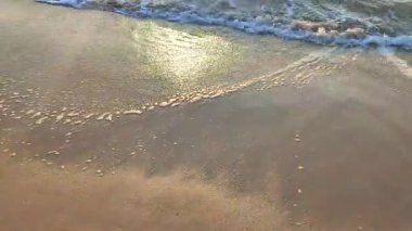 Gün batımında deniz kıyısındaki kumlu sahilde dalgalar dalgalanır. Beyaz köpüklü mavi deniz dalgaları kumsala geliyor. Deniz kıyısı kıyı şeridi. Doğal zemin, doğa zemin