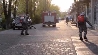 Koruyucu giysili bir adam şehrin kaldırımına antiseptik solüsyon sıkıyor. Koronavirüsü önlemek için sprey kimyasalların dezenfekte edilmesi. Halka açık yerlerde hijyenik önlemler. Koronavirüs salgını