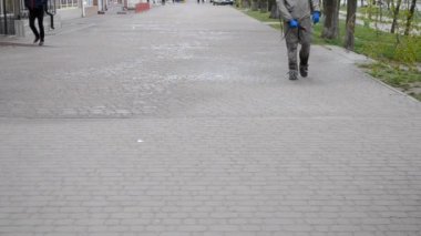 Koruyucu giysili bir adam şehrin kaldırımına antiseptik solüsyon sıkıyor. Koronavirüsü önlemek için sprey kimyasalların dezenfekte edilmesi. Halka açık yerlerde hijyenik önlemler. Koronavirüs salgını
