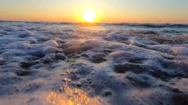 Gün doğumu, denizde gün batımı. Doğan güneş, beyaz köpükle yuvarlanan deniz dalgalarının üzerinde batıyor. Denizde gün batımı. Deniz suyu, güneş, gökyüzü. Düşük açı. Doğal doğa geçmişi. Yavaş çekim.