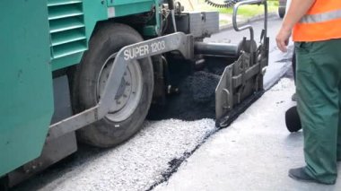 Asfalt asfalt dökerken asfalt tozu dökülüyor. Büyük kaldırım makinesi ve işçiler. Caddede asfalt gibi dönen bir makine. Aspirasyon aletleri. Püskürtme basınç makinesini çökertir