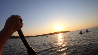 Şafak vakti SUP sörf tahtasında yüzen bir adam. Beyaz SUP tahtasının üzerinde yüzen ve günbatımında kıyıya yakın dalgalarla kürek çeken insanlar. Aktif yaşam tarzı eğlence sporu POV