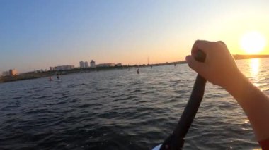 Şafak vakti SUP sörf tahtasında yüzen bir adam. Beyaz SUP tahtasının üzerinde yüzen ve günbatımında kıyıya yakın dalgalarla kürek çeken insanlar. Aktif yaşam tarzı eğlence sporu POV