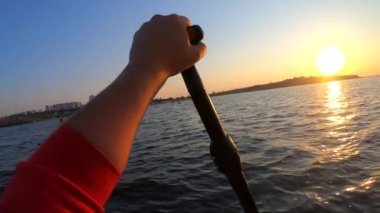 Şafak vakti SUP sörf tahtasında yüzen bir adam. Beyaz SUP tahtasının üzerinde yüzen ve günbatımında kıyıya yakın dalgalarla kürek çeken insanlar. Aktif yaşam tarzı eğlence sporu POV
