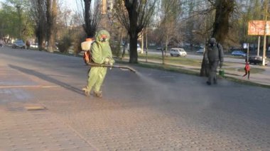 Man in airtight suit sprays disinfecting liquid a pavement on a street in the city against the backdrop of a sunset. Sanitation workers clean a crosswalk. Sanitary measures. coronavirus pandemic