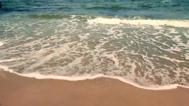 Mavi deniz, dalgalar, beyaz köpük, kumlu sahil, güneşli yaz gününde kıyılar. Beyaz köpüklü mavi deniz dalgaları kumlu deniz kıyısında güneşli bir güne çarpıyor. Deniz manzarası deniz manzarası manzarası manzarası. Yavaş çekim