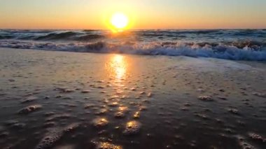 Gün doğumu, denizde gün batımı. Doğan güneş, beyaz köpükle yuvarlanan deniz dalgalarının üzerinde batıyor. Denizde gün batımı. Deniz suyu, güneş, gökyüzü. Düşük açı. Doğal doğa geçmişi. Yavaş çekim.