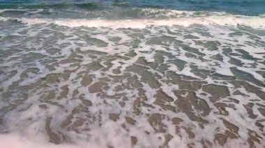 Mavi deniz, dalgalar, beyaz köpük, kumlu sahil, güneşli yaz gününde kıyılar. Beyaz köpüklü mavi deniz dalgaları kumlu deniz kıyısında güneşli bir güne çarpıyor. Deniz manzarası deniz manzarası manzarası manzarası. Yavaş çekim