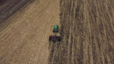 Traktör toprağı sürüyor. Sonbahar günü buğday hasadından sonra sarı tarlada toprağı süren yeşil traktörün üzerinde uçmak. Traktör kazıyor. Sahada tarım işi. Hava aracı görünümü
