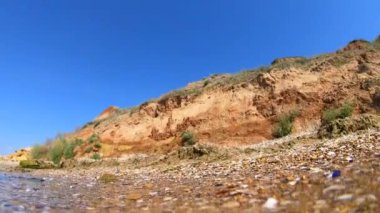 Deniz kıyısının kumlu sahilinde, saydam suyun altından, dağ ve mavi gökyüzü manzarası. Güneşli bir yaz günü. Açı altı geniş. İçerideki deniz dalgaları hareket ediyor. Doğa geçmişi. Sudaki dalgalar
