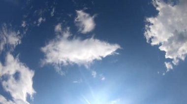 Fast moving white cumulus clouds across the blue sky and shining sun. Sunlight, sun beams. Wide angle. Bottom view. Sky landscape. Environment atmosphere weather. Natural background. Nature backdrop.