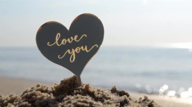 Plastik kalp şeklinde kelimeler. Güneşli yaz günlerinde arka plandaki deniz dalgalarının kumlu sahillerinde seni seviyorum. Aşk ilişkisi romantizmi Aziz Sevgililer Günü kutlaması olarak kabul et.